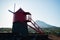 A restored traditional Pico Island red windmill silhouetted with the sun directly behind it