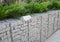 Retaining wall design: modern gabion wire mesh wall fence full with stones and outdoor lightning installed on the top