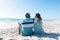 Retired african american senior couple sitting on sand at beach with copy space over blue sky