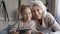 Retired grandmother and little granddaughter relax on pillows hold tablet