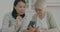 Retired lady learning to use smartphone application talking to young woman volunteer in kitchen at home