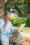 Retired man leaning against tree with a laptop