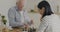 Retired man playing chess with young woman volunteer enjoying game and talking in kitchen at home