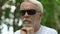 Retired man with visual impairment resting on bench in park leaning on cane