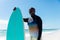 Retired senior african american man holding surfboard standing at beach against blue sky