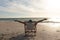 Retired senior biracial man with arms outstretched sitting on folding chair at beach during sunset