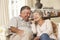 Retired Senior Couple Sitting On Sofa Talking On Phone At Home Together