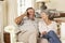 Retired Senior Couple Sitting On Sofa Talking On Phone At Home Together