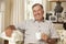 Retired Senior Man Sitting On Sofa Drinking Tea At Home