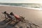 Retired senior multiracial couple relaxing while sitting on folding chairs at beach during sunset