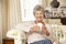 Retired Senior Woman Sitting On Sofa Drinking Tea At Home