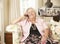 Retired Senior Woman Sitting On Sofa At Home On Phone