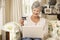Retired Senior Woman Sitting On Sofa At Home Using Laptop To Make Online Purchase