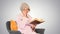 Retired woman reading a book sitting on a chair on gradient back