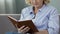 Retired woman sitting on couch and reading book, avid book reader, leisure time