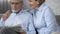 Retiree husband reading newspaper on sofa, woman beside hugging him, love