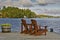 Retirement Living - Two Muskoka chairs sitting on a boat dock facing a calm lake with trees and cottages in the background