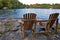 Retirement Living - Two Muskoka chairs sitting on a rocky shore facing a calm lake with cottages in the background