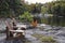 Retirement Living - Two Muskoka chairs sitting on a rocky shore facing a calm lake with trees and a white cottage in the backgroun