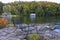 Retirement Living - Two outdoor chairs sitting on a rocky shore facing a calm lake with trees and a white cottage in the backgroun