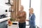 Retirement senior couple laughing, standing on bright kitchen together