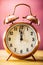 Retro alarm clock with two minutes to midnight. Filtered photo in vibrant colors 50s to 60s. Pink background