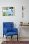 Retro blue armchair, vintage wooden beige table & pendulum clock over off white wall, tiled beige floor and orange ornate carpet