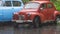 Retro car standing in rain on background of green trees. Action. Small retro car stands under downpour in nature