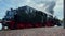 Retro German coal steam locomotive with thick clouds of steam leaving station