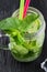 Retro glass jar of lemonade with cucumber and mint on wooden table. Cubes of ice