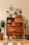 Retro interior design of art workshop room with wooden vintage bureau and chair, cube, plants, cacti, books, photos.