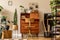 Retro interior design of art workshop room with wooden vintage bureau and chair, shelf plants, cacti, books, photos .