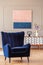 Retro, navy blue armchair in an elegant living room interior with an abstract painting on a wall