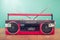 Retro outdated portable stereo boombox radio receiver with cassette recorder from circa late 70s front aquamarine wall background.