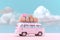 Retro pink minivan with colored suitcases on the roof trunk. Vintage car on a background of blue sky with lush clouds. Generated