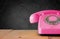 Retro pink telephone on wooden table and blackboard Background