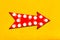 Retro red arrow shaped vintage colorful illuminated metallic display direction sign with glowing light bulbs on vivid yellow wall