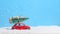 Retro red toy car carrying christmas tree on roof in the snow on blue background. Christmas background. Holidays card