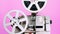 Retro reel with film rotating on pink studio background. Old-fashioned 8mm film projector playing. Vintage movie objects