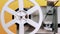 Retro reel with film rotating on yellow studio background. Old-fashioned 8mm film projector playing. Vintage movie