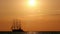 Retro sailboat ship with long mast sailing away on horizon during sea sunset