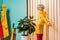 retro styled woman standing at ficus plant in flowerpot at colorful apartment doll