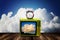 Retro television and alarm clock on deck with clouds background