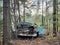 Retro turquoise car crash in woodlands surrounded by tall conifers