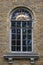 Retro window in brick house with marble ledge and cracked paint, with lit chandelier showing through top arched stained glass