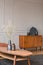 Retro wooden cabinet with black vases in the corner of classy grey living room interior with ginger sofa