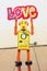 Retro yellow robot man holding up a bright and colorful cloth love sign