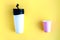 Reusable black and white takeaway coffee cup with disposable paper cup isolated on yellow background