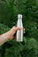 Reusable stainless thermos bottle for water in female hand to replenish the body`s water reserves against the background of fern