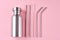 Reusable steel straws and aluminium bottle on pink background